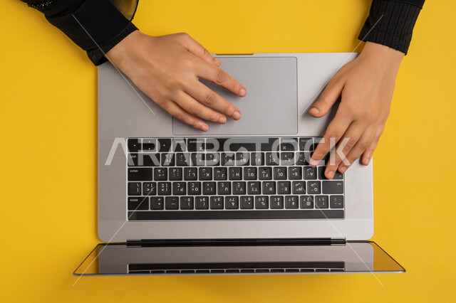 دمج التكنولوجيا الحديثة في الحياة العملية، إنجاز المهام المطلوبة عن بعد، بورتريه علوي عامودي لايدي امرأة عربية خليجية اماراتية تعمل على الحاسب المحمول، شابة سعودية ترتدي العباءة تقوم بالكتابة على لوحة المفاتيح، مفهوم ادارة الاعمال وتحقيق الأهداف، خلفية صفراء