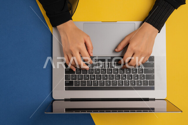 Integrating modern technology into business life, accomplishing required tasks remotely, vertical overhead portrait of a Gulf Arab Emirati woman working on laptop, young Saudi woman wearing abaya typing on keyboard, concept of business management and achieving goals, colorful background
