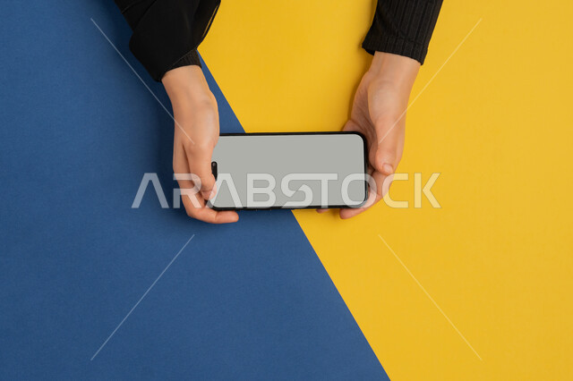 E-marketing for applications, blank gray screen display, integration of modern technology into daily and work life, vertical overhead portrait of a Saudi Arabian Gulf woman providing mobile services, young Emirati woman using a mobile phone, colorful background