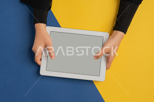 متابعة الدروس التعليمية، الاستمتاع بمشاهدة الافلام، بورتريه علوي عامودي لايدي امرأة عربية خليجية سعودية تقوم بالنقر على جهاز التابلت، شابة اماراتية تلعب الالعاب الفيديو الالكترونية، استخدام التقنيات الحديثة، عرض شاشة رمادية فارغة، خلفية ملونة