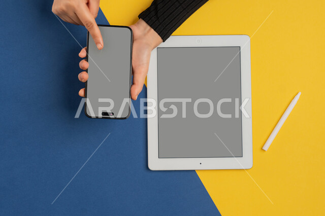 التسويق الالكتروني للتطبيقات، عرض شاشة رمادية فارغة، دمج التكنولوجيا الحديثة في الحياة اليومية والعملية، بورتريه علوي عامودي لايدي امرأة عربية خليجية سعودية تنقر على شاشة الهاتف المحمول، شابة اماراتية تقوم باستخدام جهاز التابلت، خلفية ملونة