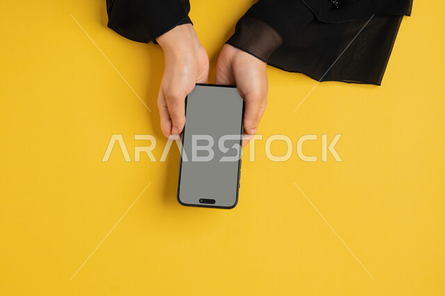 عرض شاشة رمادية فارغة، التسويق الالكتروني للتطبيقات، دمج التكنولوجيا الحديثة في الحياة اليومية والعملية، بورتريه علوي عامودي لايدي امرأة عربية خليجية سعودية تقوم بتقديم خدمات الموبايل، شابة اماراتية تستخدام الهاتف المحمول، خلفية صفراء