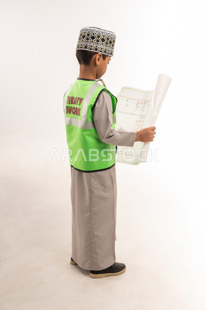 Auditing and following up on engineering projects and plans, the concept of work in the engineering sector, choosing and determining the future profession from a young age, portrait from the back of a smiling Gulf Arab Omani boy wearing a sleeve and a protective vest holding a plan in his hand, full body length, white background