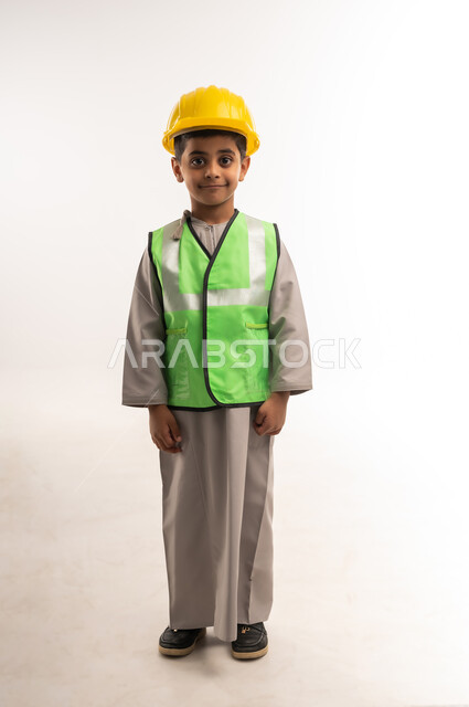 اختيار وتحديد المستقبل منذ الصغر، مفهوم العمل في القطاع الهندسي، ايماءات الشغف لتحقيق حلم الطفولة، بورتريه لولد عربي خليجي عماني مبتسم يرتدي الستره وخوذة الحماية يقف بإستقامة وينظر إلى الكاميرا بتعابير السعادة والسرور، الطول الكامل للجسم، خلفية بيضاء