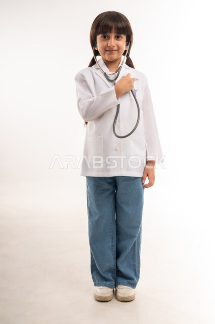قياس نبضات القلب باستخدام السماعات الطبية، أهداف و طموحات للمستقبل، اختيار المهنه المستقبلية منذ الصغر، الاجتهاد والسعي لتحقيق حلم الطفولة، بورتريه لفتاة عربية خليجية عمانية ترتدي المعطف الأبيض، بنت سعودية تقف باستقامة، الطول الكامل للجسم، خلفية بيضاء
