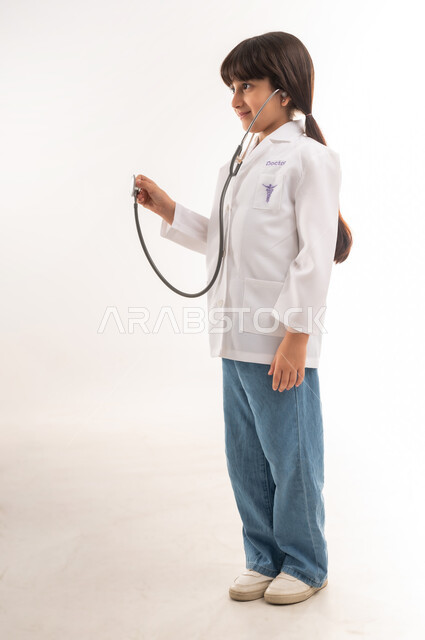 اختيار المهنه المستقبلية منذ الصغر، طموحات وأهداف للمستقبل، قياس نبضات القلب باستخدام السماعات الطبية، الاجتهاد والسعي لتحقيق حلم الطفولة، بورتريه لفتاة عربية خليجية عمانية ترتدي المعطف الأبيض، بنت سعودية تقف باستقامة، الطول الكامل للجسم، خلفية بيضاء