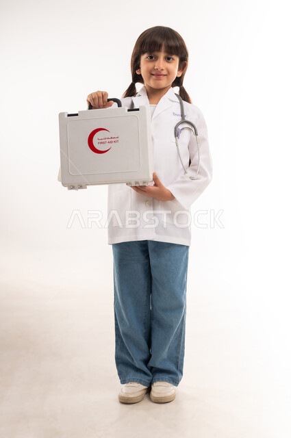 مساعدة المرضى في الحالات الطارئة، الأهداف والطموحات المستقبلية بالعمل في المستشفيات، بورتريه لفتاة عربية خليجية عمانية ترتدي المعطف الأبيض والسماعات الطبية، بنت سعودية تحمل حقيبة الاسعافات الاولية، الحلم بالحصول على مهنة الطب, الجسم بالطول الكامل، خلفية بيضاء