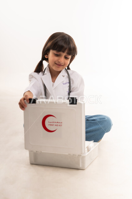 مساعدة المرضى في الحالات الطارئة، السعي للحصول على مهنة الطب, الطموحات المستقبلية بالعمل في المستشفيات، بورتريه لفتاة عربية خليجية عمانية ترتدي المعطف وسماعة الطبيب، بنت سعودية تجلس وتقوم بفتح حقيبة الاسعافات الاولية، خلفية بيضاء