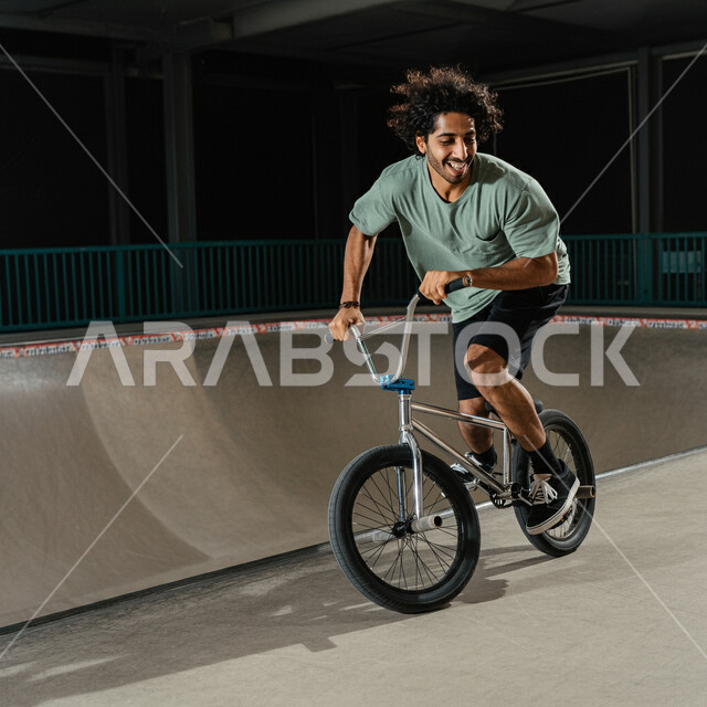 ممارسة هواية ركوب الدراجة الهوائية، شاب عربي خليجي سعودي يرتدي الزي الرياضي الخاص يركب على العجلة وينطلق بسرعة في الطرقات، المشاركة في المسابقات والمنافسات بإيماءات السعادة والتحدي، نشاط بدني للمحافظه على الصحه و اللياقه الجسديه