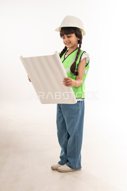 العمل في القطاع الهندسي، تدقيق ومراجعة المخططات الهندسية، تحديد واختيار المستقبل منذ الصغر، بنت سعودية بايماءات الشغف لتحقيق حلم الطفولة، بورتريه لفتاة عربية خليجية عمانية ترتدي الستره وخوذة الحماية وتحمل مخطط المشروع، الطول الكامل للجسم، خلفية بيضاء