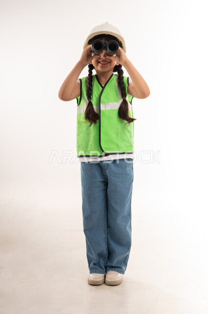 مفهوم العمل في القطاع الهندسي، السعي للأهداف والطموحات المستقبلية، رؤية الاشياء البعيدة، بورتريه لفتاة عربية خليجية عمانية ترتدي سترة الحماية وتمسك بيدها منظار الرؤية ثنائي العينين لمشاهدة شيئا ما، بنت سعودية تنظر عبر التلسكوب، الطول الكامل للجسم، خلفية بيضاء