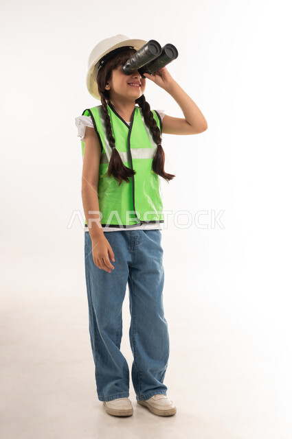 السعي للأهداف والطموحات المستقبلية، رؤية الاشياء البعيدة، بورتريه لفتاة عربية خليجية عمانية ترتدي سترة الحماية وتمسك بيدها منظار الرؤية ثنائي العينين لمشاهدة شيئا ما، بنت سعودية تنظر عبر التلسكوب، مفهوم العمل في القطاع الهندسي، الطول الكامل للجسم، خلفية بيضاء