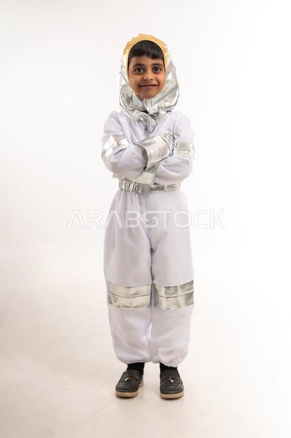 الشغف والجد لتحقيق الأهداف في المستقبل، التطور ودعم قطاع الفضاء في سلطنة عمان، بورتريه لفتى عربي خليجي عماني مبتسم يرتدي زي رائد الفضاء، صبي سعودي ينظر إلى الكاميرا ويقف باستقامة وأيدي متقاطعة، حلم الوصول إلى القمر، الطول الكامل للجسم، خلفية بيضاء