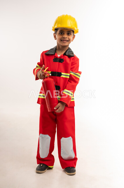 اختيار وتحديد مهنة المستقبل، مفهوم العمل في مجال الانقاذ والحمايه المدنية، آمال وأمنيات لمهن و وظائف مستقبلية، بورتريه لولد عربي خليجي عماني يرتدي الخوذة و سترة الحماية الخاصة برجال الإطفاء، صبي سعودي يحمل بيديه مطفأة الحريق, صورة الجسم بالطول الكامل، خلفية بيضاء