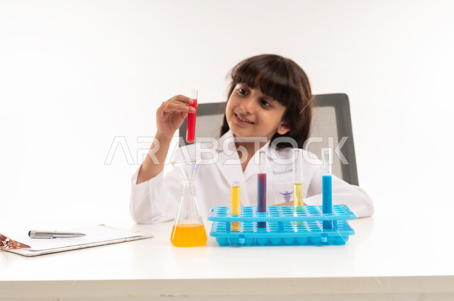 A dream to become a chemical researcher, choosing and determining a future career since childhood, conducting experiments and biochemical reactions in the laboratory, portrait of an Arab Gulf Omani girl wearing a white coat and using test tubes, a Saudi girl conducting scientific research in a chemistry laboratory, white background