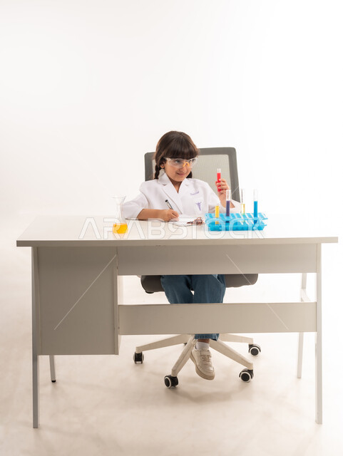 Choosing and determining the future profession since childhood, the wish to obtain the profession of a chemical researcher, conducting experiments and biochemical reactions in the laboratory, a portrait of an Arab Gulf Omani girl wearing a white coat and using test tubes, a Saudi girl conducting scientific research in the chemistry laboratory, white background