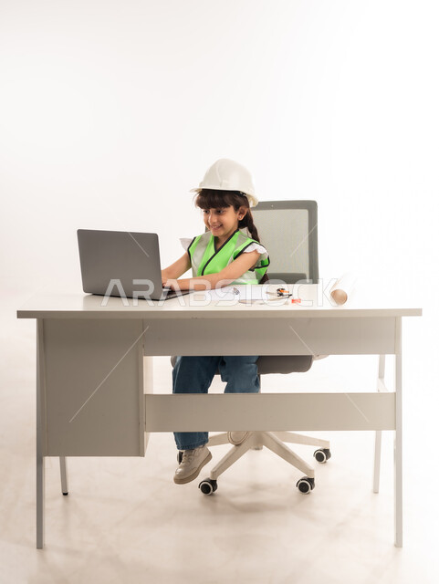 اختيار المستقبل منذ الصغر، العمل في القطاع الهندسي في سلطنة عمان، استخدام الاجهزة التقنية الحديثة في القطاع الهندسي، بنت سعودية بايماءات الشغف لتحقيق حلم الطفولة، بورتريه لفتاة عربية  خليجية عمانية ترتدي الستره تجلس امام الطاولة تستخدم الحاسوب المحمول، حلفية بيضاء