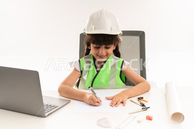العمل في القطاع الهندسي في سلطنة عمان، اختيار المستقبل منذ الصغر، استخدام الاجهزة التقنية الحديثة في القطاع الهندسي، بنت سعودية بايماءات الشغف لتحقيق حلم الطفولة، بورتريه لفتاة عربية  خليجية عمانية ترتدي الستره تجلس امام الطاولة تستخدم الحاسوب المحمول، حلفية بيضاء