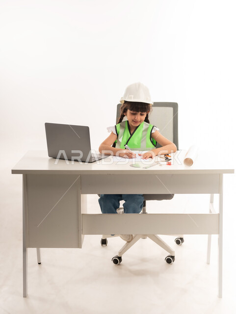 العمل في القطاع الهندسي في سلطنة عمان، اختيار المستقبل منذ الصغر، استخدام الاجهزة التقنية الحديثة في القطاع الهندسي، بنت سعودية بايماءات الشغف لتحقيق حلم الطفولة، بورتريه لفتاة عربية  خليجية عمانية ترتدي الستره تجلس امام الطاولة تستخدم الحاسوب المحمول، حلفية بيضاء