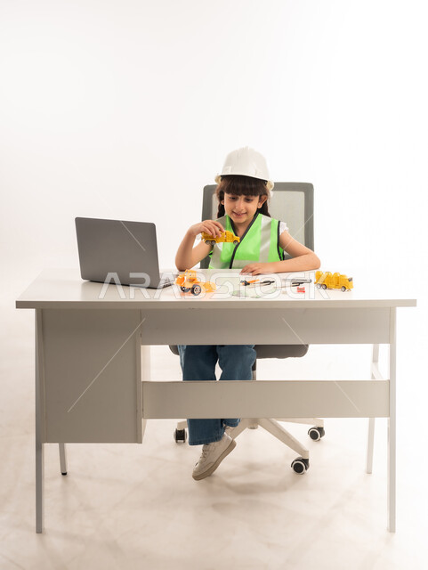 العمل في القطاع الهندسي في سلطنة عمان، اختيار المستقبل منذ الصغر، استخدام الاجهزة التقنية الحديثة في القطاع الهندسي، بنت سعودية بايماءات الشغف لتحقيق حلم الطفولة، بورتريه لفتاة عربية  خليجية عمانية ترتدي الستره تجلس امام الطاولة تستخدم الحاسوب المحمول، حلفية بيضاء