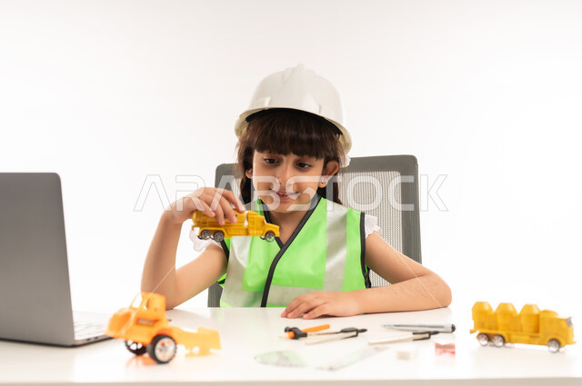 Choosing the future since childhood, working in the engineering sector in the Sultanate of Oman, using modern technical devices in the engineering sector, a Saudi girl with gestures of passion to achieve her childhood dream, a portrait of an Arab Gulf Omani girl wearing a jacket sitting in front of a table using a laptop, a white veil