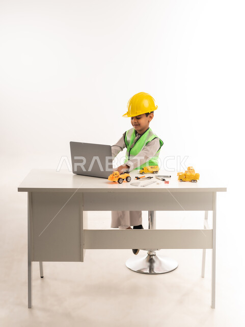 Choosing and determining the future from a young age, working in the engineering sector in the Sultanate of Oman, using modern technical devices in the engineering sector, gestures of passion to achieve a childhood dream, portrait of an Arab Gulf Omani boy wearing a dishdasha and a jacket sitting in front of a table using a laptop, white scarf