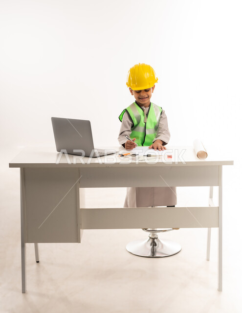 اختيار وتحديد المستقبل منذ الصغر، العمل في القطاع الهندسي في سلطنة عمان، استخدام الاجهزة التقنية الحديثة في القطاع الهندسي، ايماءات الشغف لتحقيق حلم الطفولة، بورتريه لولد عربي خليجي عماني يرتدي الدشداشة والستره يجلس امام الطاولة يستخدم الحاسوب المحمول، حلفية بيضاء