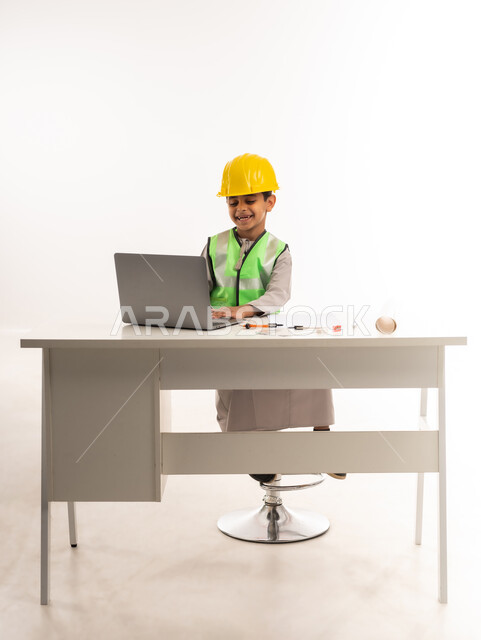 اختيار وتحديد المستقبل منذ الصغر، العمل في القطاع الهندسي في سلطنة عمان، استخدام الاجهزة التقنية الحديثة في القطاع الهندسي، ايماءات الشغف لتحقيق حلم الطفولة، بورتريه لولد عربي خليجي عماني يرتدي الدشداشة والستره يجلس امام الطاولة يستخدم الحاسوب المحمول، حلفية بيضاء