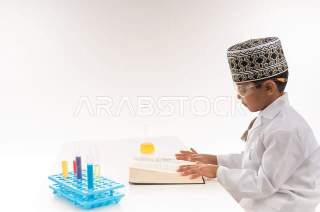 Using test tubes and writing down the results in a notebook, the profession of a bio-laboratory specialist, choosing and determining the future from a young age, a portrait of an Arab Gulf Omani boy wearing a turban and a white coat sitting in front of a table wearing protective glasses to conduct chemical reactions, white background