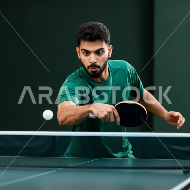 Practicing fun sports and physical activities, a young Saudi Arabian Gulf man wearing sportswear holding a table tennis racket, playing with speed and high concentration, maintaining sports and physical fitness, enjoying friendly matches and local tournaments
