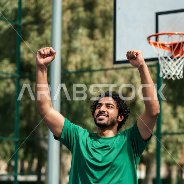 الشغف بالألعاب الرياضية, إقامة المباريات الودية التنافسية، المشاركة في البطولات والدوريات المحلية، ممارسة هواية كرة السلة, صورة مقربة لرجل عربي خليجي سعودي يرتدي زي رياضي يرفع يديه بإيماءات الحماس والسعادة لتسجيله الرمية، أنشطة ترفيهية رياضية للشباب بالسعودية