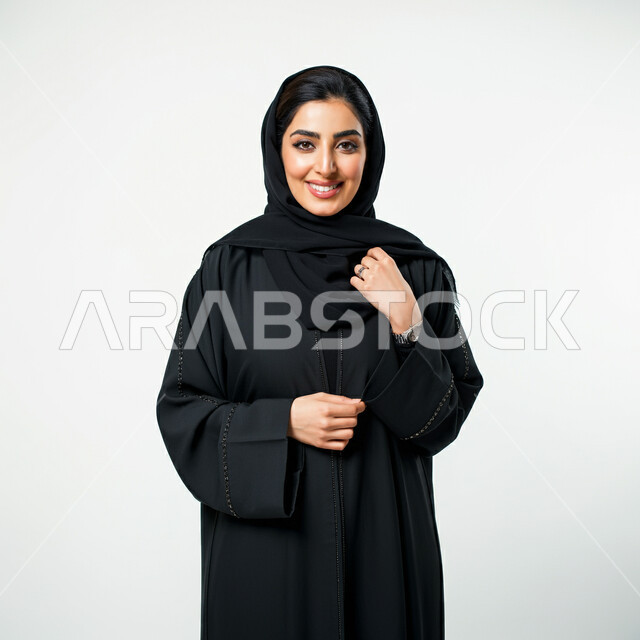 مفهوم الأناقة والأنوثة, تعابير السرور والسعادة، التقاط صور شخصية للوثائق الرسمية، بورتريه لامرأة عربية خليجية سعودية ترتدي الحجاب والعباءة تنظر إلى الكاميرا بايماءات الثقة بالنفس, الاهتمام بالمظهر الخارجي، خلفية بيضاء