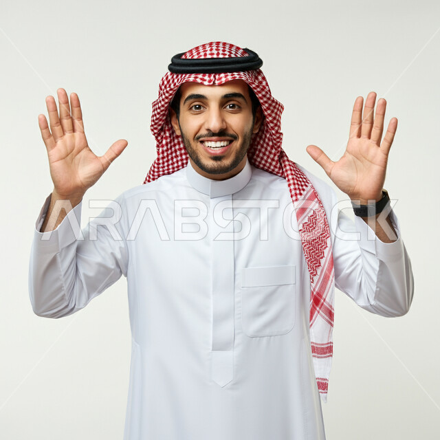 تعابير الانتهاء من أمر ما، بورتريه لرجل عربي خليجي سعودي مبتسم يرفع يديه للأعلى ينظر إلى الكاميرا بإيماءات السرور والسعادة، مفهوم الأناقة والوسامة، الشعور بالفرح للقيام بالواجبات المطلوبة، خلفية بيضاء