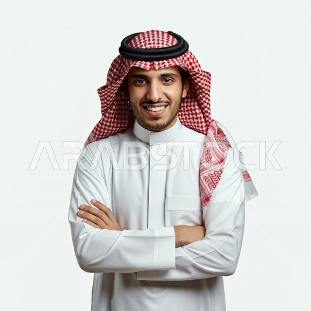 مفهوم الأناقة والوسامة، الوقوف بيدين متقاطعتين بتعابير الثقة بالنفس، بورتريه لرجل عربي خليجي سعودي يرتدي الثوب التقليدي والشماغ ينظر إلى الكاميرا بإيماءات البشاشة والسرور، الاهتمام بالمظهر الخارجي، خلفية بيضاء