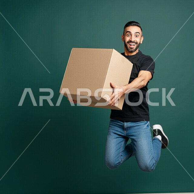 Overwhelmed with happiness of getting the package quickly, easy delivery of orders to customers, ordering products online, online shopping, portrait of a young Saudi Arabian Gulf man in casual clothes holding the box in his hands and jumping with joy and happiness, green background