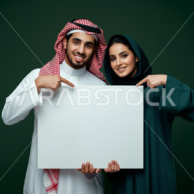 Using illustrations and educational tools, advertisements and marketing presentations, portrait of a Saudi Arabian Gulf man and woman wearing traditional clothes holding a rectangular mockup, pointing with index finger at an empty white billboard, looking at the camera with expressions of pleasure and happiness, gray background