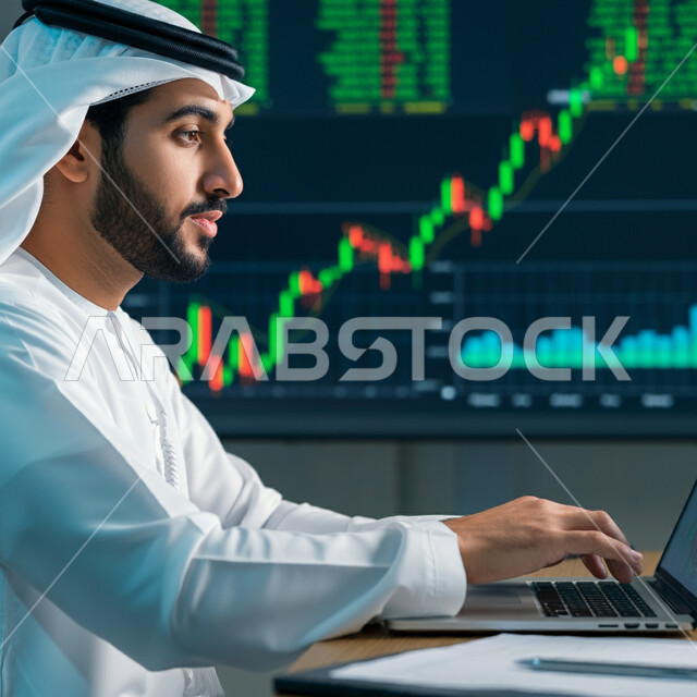 مراقبة الرسوم البيانية الهولوجرامية على الشاشات الإلكترونية المضيئة، متابعة ارتفاع وانخفاض الأسهم في سوق البورصة، صورة مقربة من الجانب لرجل أعمال عربي خليجي سعودي يرتدي الثوب التقليدي والغترة يقوم بالعمل على الحاسوب المحمول، استخدام الأجهزة التقنية الحديثة