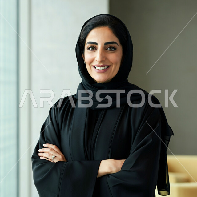 The concept of femininity and softness, interest in elegance and external appearance, a close-up image of a smiling Saudi Arabian Gulf woman wearing a black abaya looking at the camera with expressions of pleasure and self-confidence, standing with crossed hand gestures