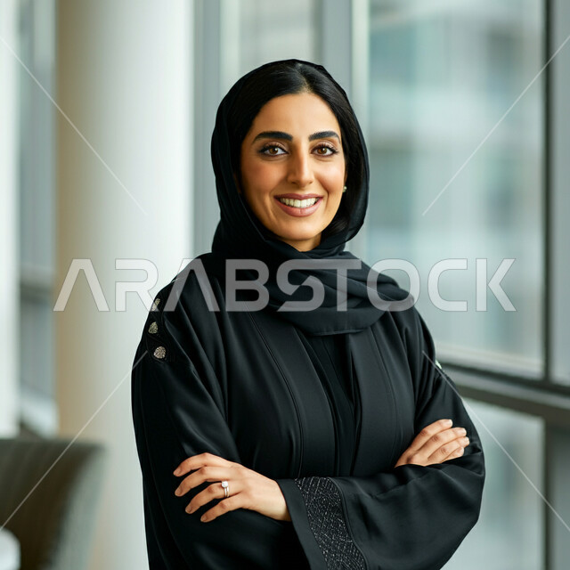 مفهوم الانوثة والنعومة، الاهتمام بالاناقة والمظهر الخارجي، صورة مقربة لامرأة عربية خليجية سعودية مبتسمة ترتدي العباءة السوداء تنظر الى الكاميرا بتعابير السرور والثقة بالنفس، الوقوف بايماءات ايدي متقاطعة