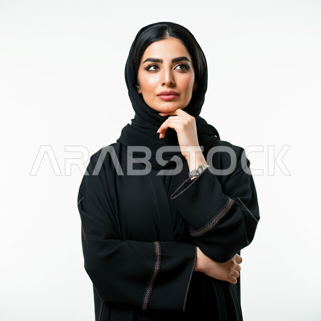 Trying to find a solution to something, contemplation, focus and planning for the future, the concept of femininity and softness, interest in elegance and outward appearance, close-up portrait of a veiled Saudi Arabian Gulf woman wearing a black abaya, putting her hand on her chin and looking away with gestures of thinking and contemplation, white background