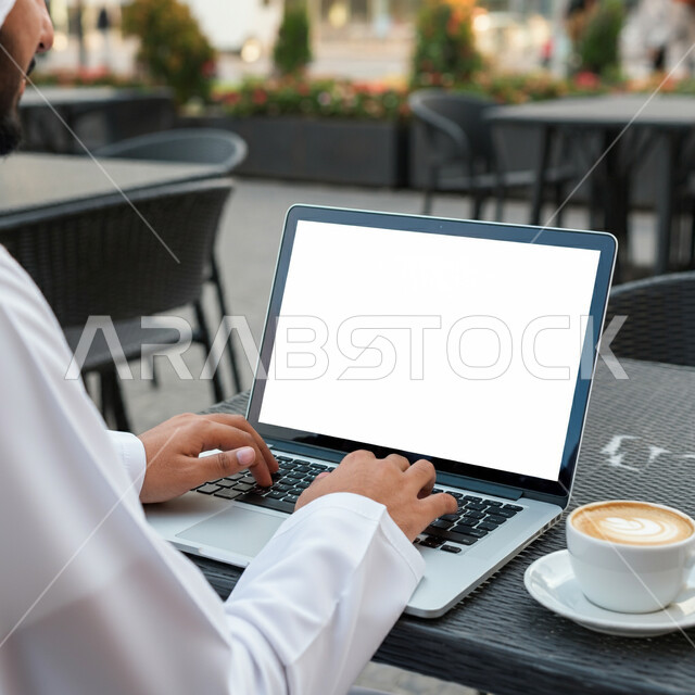 الاستمتاع بالمشروبات الساخنة في أحد المقاهي، تصفح التطبيقات والبرامج الالكترونية عبر الابتوب, استخدام الأجهزة التقنية الحديثة والمتطورة, إدراة الأعمال عن بعد, رجل عربي خليجي سعودي يرتدي الثوب التقليدي والشماغ يعمل على جهاز الحاسب المحمول، عرض شاشة بيضاء فارغة