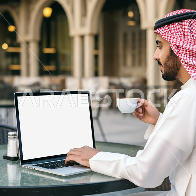 الاستمتاع بالمشروبات الساخنة في أحد المقاهي، تصفح التطبيقات والبرامج الالكترونية عبر الابتوب, استخدام الأجهزة التقنية الحديثة والمتطورة, إدراة الأعمال عن بعد, رجل عربي خليجي سعودي يرتدي الثوب التقليدي والشماغ يعمل على جهاز الحاسب المحمول، عرض شاشة بيضاء فارغة