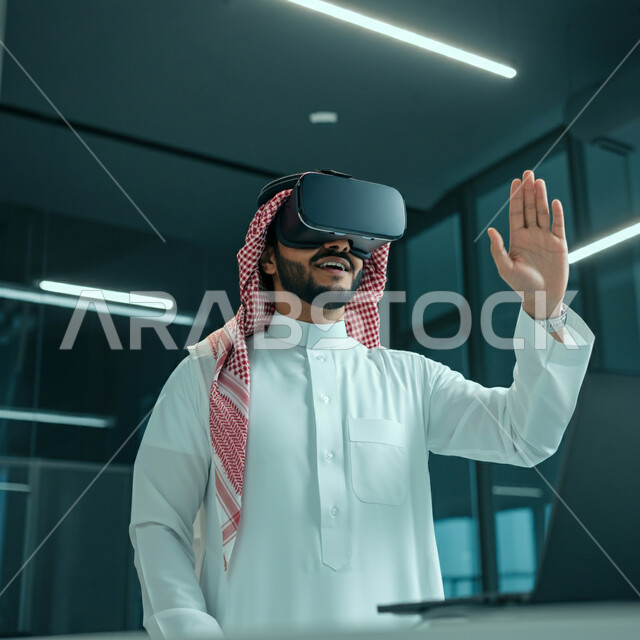 Interaction, integration and simulation of the imaginary world, a smiling Saudi Arabian Gulf man wearing the traditional thobe and shemagh, wearing virtual reality glasses, raising his palms up to try to touch something, gestures of prohibition and stopping doing something, fun and entertainment watching through 3D glasses