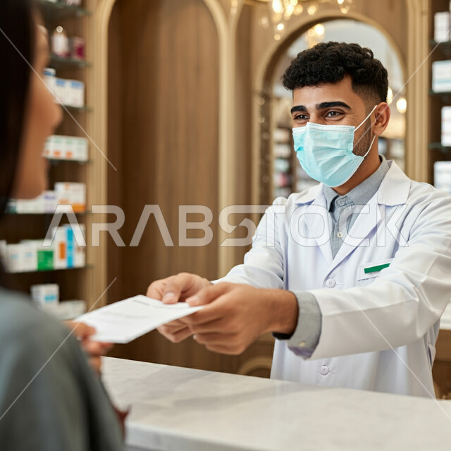 أداء الواجبات المهنية بجودة عالية، صرف العقاقير الموجودة في الوصفات الطبية ، توفير وتجهيز الادوية اللازمة للمريضة، استقبال المرضى وتقديم العلاج اللازم،  صيدلي عربي خليجي سعودي يرتدي الكمامة الطبية للوقاية من فايروس كورونا، مفهوم الصيدلة والرعاية الصحية