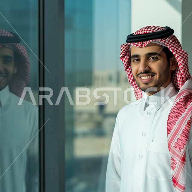 مفهوم الاناقة والرجولة والقوة، الشياكة والاهتمام بالمظهر الخارجي، رجل عربي خليجي سعودي مبتسم يرتدي الثوب التقليدي والشماغ ينظر الى الكاميرا بتعابير الفرح والسرور، الوقوف باستقامة واعتدال، تعابير السعادة والثقة بالنفس