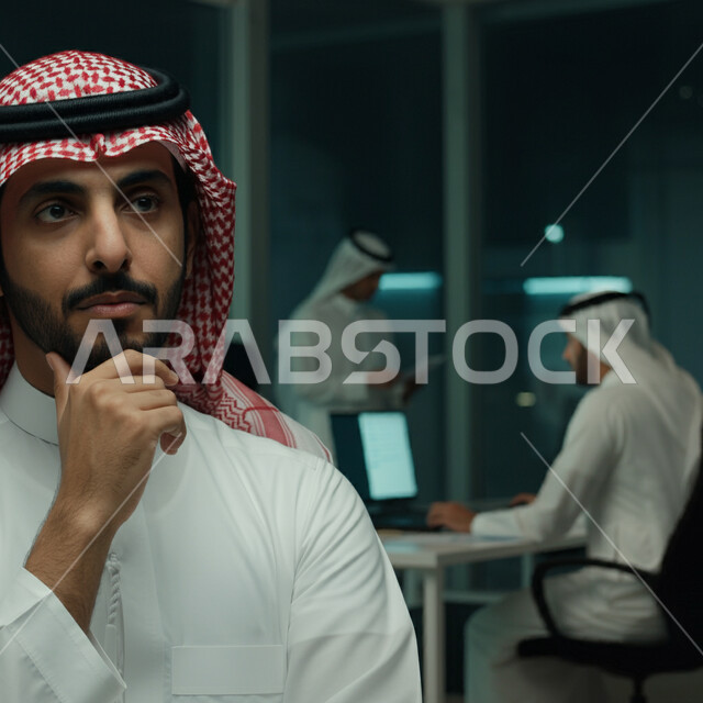 التمعن والتركيز لإيجاد حل للمشكلة، صورة مقربة لرجل عربي خليجي سعودي يرتدي الثوب التقليدي والشماع يضع يده على ذقنه بتعابير التفكير والتركيز بشيء ما داخل مقر الشركة، ايماءات شرود الذهن والقلق، التأمل و التخطيط للمستقبل، العمل في شركات المملكة العربية السعودية