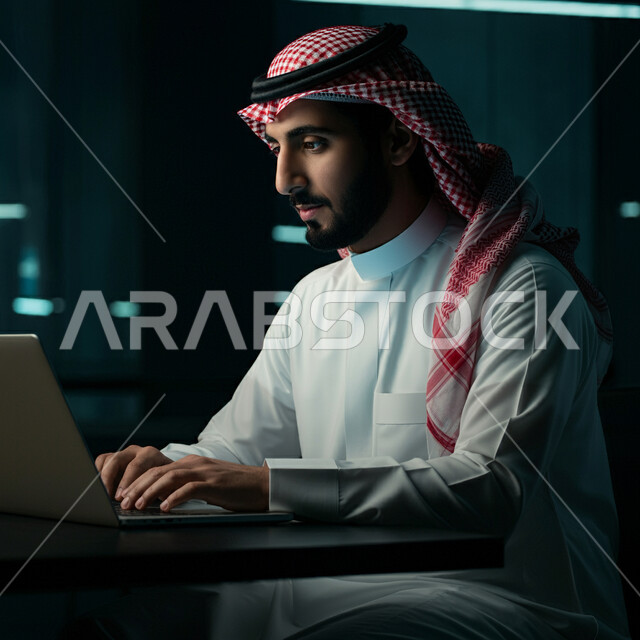 أداء المهام والاعمال المكتبية داخل مقر الشركة، صورة من الجانب لرجل عربي خليجي سعودي يرتدي الثوب التقليدي والشماغ  يجلس امام مكتبه يقوم بالعمل على الحاسب المحمول، دمج التقنية الحديثة والتكنولوجيا في الحياة العملية، العمل في مكاتب وشركات المملكة العربية السعودية