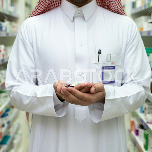 ادوية لمعالجة الحالات المرضية والوقاية من الامراض، مفهوم الصيدلة والمستلزمات الطبية، الطب والرعاية الصحية، صورة مقربة لطبيب عربي خليجي سعودي يرتدي الثوب التقليدي والشماغ يمسك بيده جرعة دواء خاصة بالمريض، العمل في القطاع الصحي