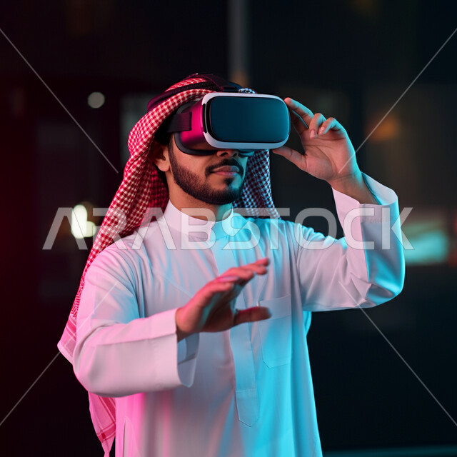 الاندماج ومحاكاة العالم الخيالي، بورتريه لرجل عربي خليجي سعودي يرتدي الثوب التقليدي والشماغ يضع نظارة الواقع الافتراضي يرفع يديه للاعلى بايماءات صد شيء ما والدفاع عن النفس، دمج التسلية بالتقنية والتكنولوجيا، قضاء اوقات ممتعة في عطلة نهاية الاسبوع، خلفية ملونة