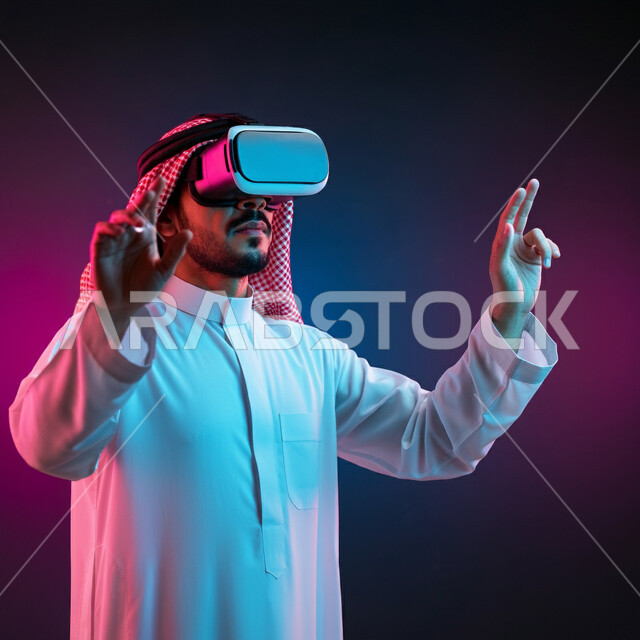 الاندماج ومحاكاة العالم الخيالي، بورتريه لرجل عربي خليجي سعودي يرتدي الثوب التقليدي والشماغ يضع نظارة الواقع الافتراضي يرفع يديه للاعلى بايماءات صد شيء ما والدفاع عن النفس، دمج التسلية بالتقنية والتكنولوجيا، قضاء اوقات ممتعة في عطلة نهاية الاسبوع، خلفية ملونة
